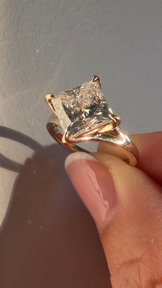 Rose gold engagement ring with a square princess cut diamond held by a finger