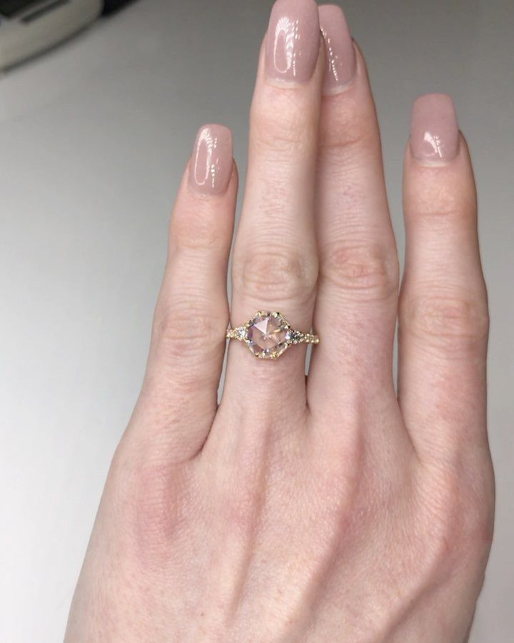 Gold engagement ring with a rose-cut diamond on a finger with nude nails.