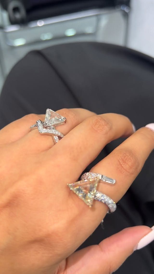 Two silver rings with triangular trillion-cut diamonds worn on a person's fingers.