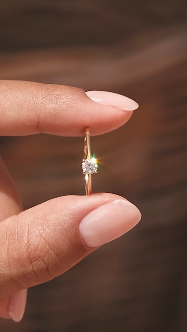 Gold solitaire engagement ring with a single diamond held between two fingers.