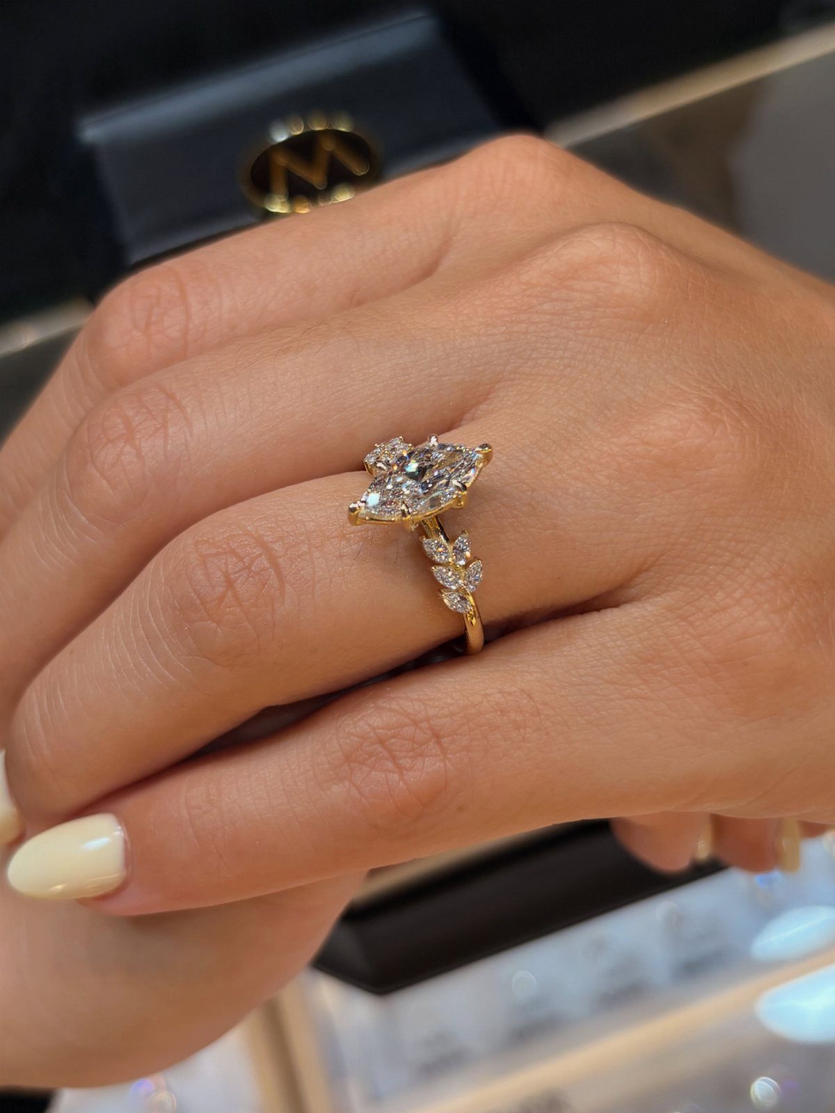 Gold engagement ring with pear-shaped diamond and side stones on a finger