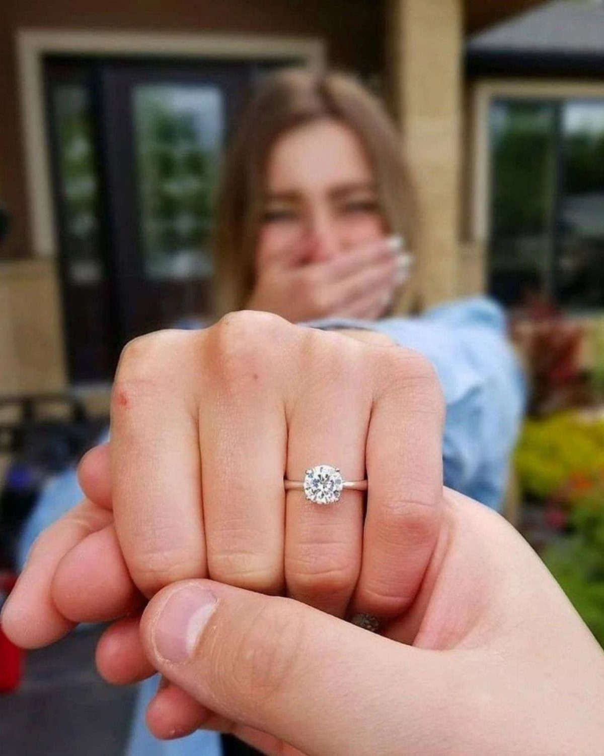 Silver engagement ring with a round diamond on a hand holding another hand.