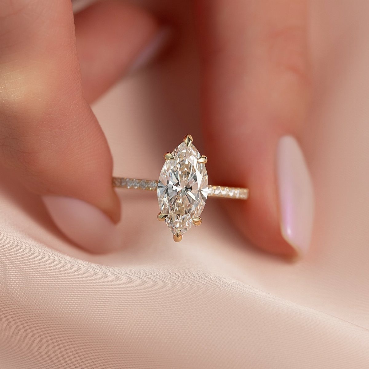 Gold engagement ring with marquise diamond and pavé band held by fingers