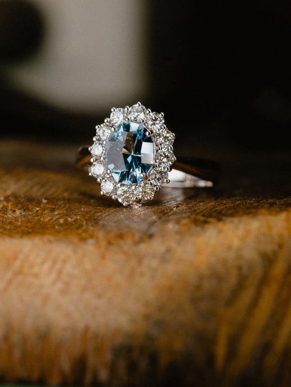 Silver engagement ring with oval blue gemstone and diamond halo on wooden surface