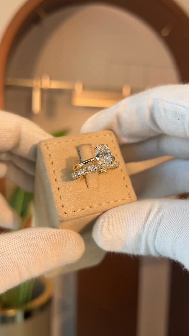 Two gold diamond rings displayed in a beige box held by gloved hands.