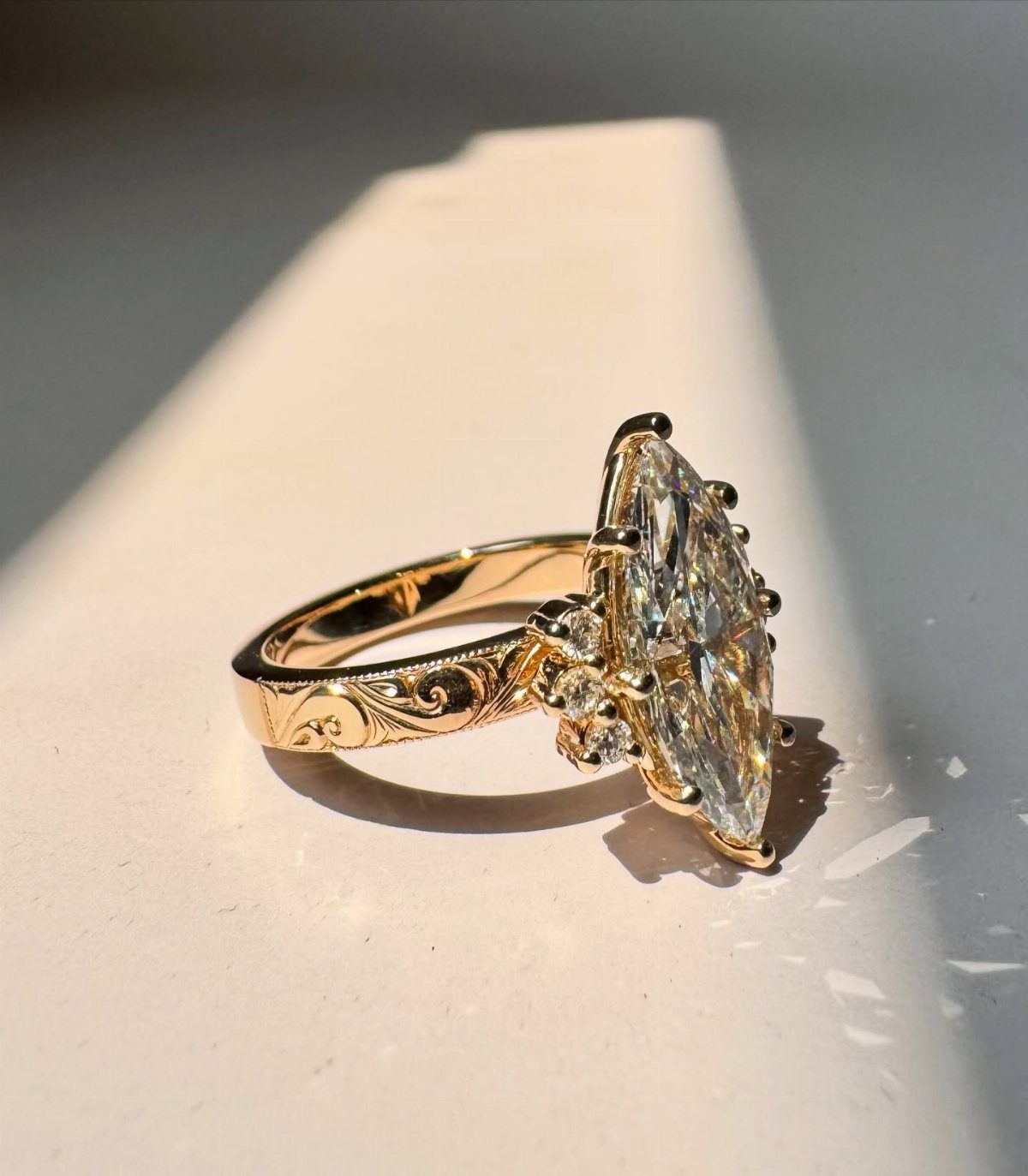 Gold engagement ring with marquise diamond and ornate floral engravings on the band