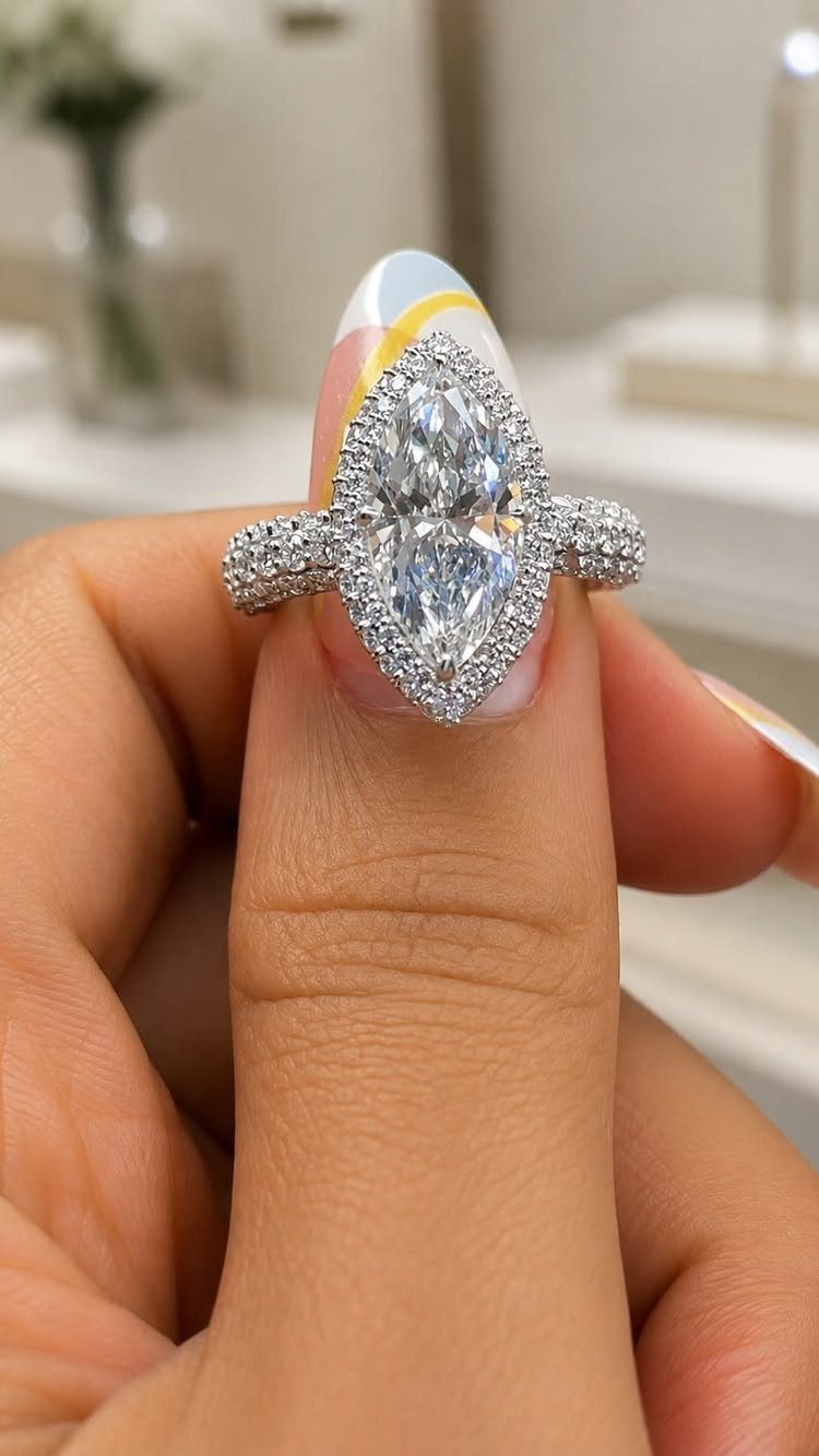Marquise-cut diamond engagement ring on a woman's finger with colorful nail art.