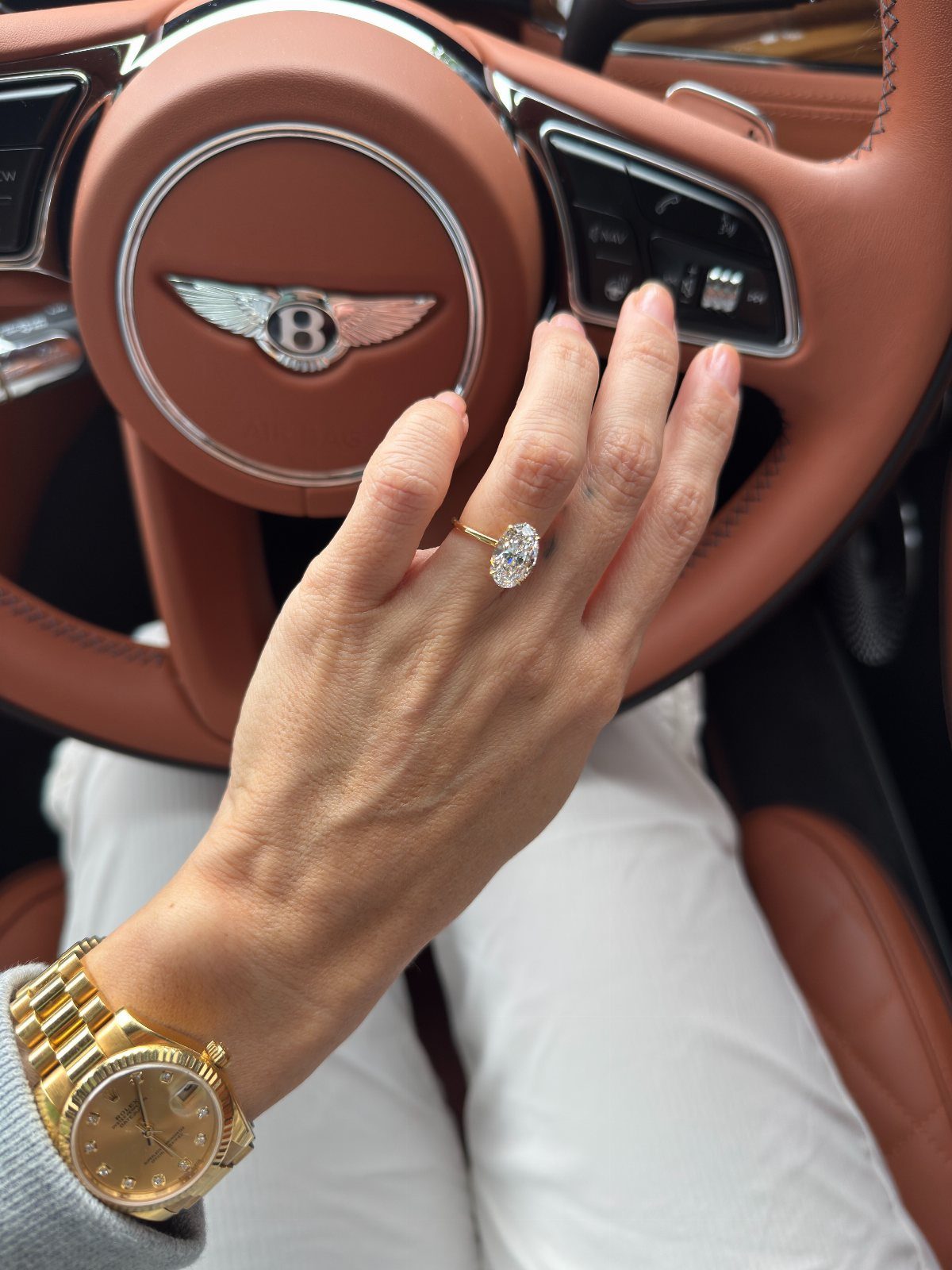 Woman's hand with oval diamond engagement ring on a brown leather steering wheel