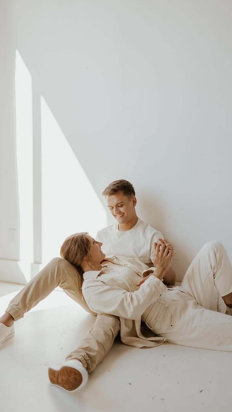 Couple in neutral cream and white outfits sitting on a white floor.