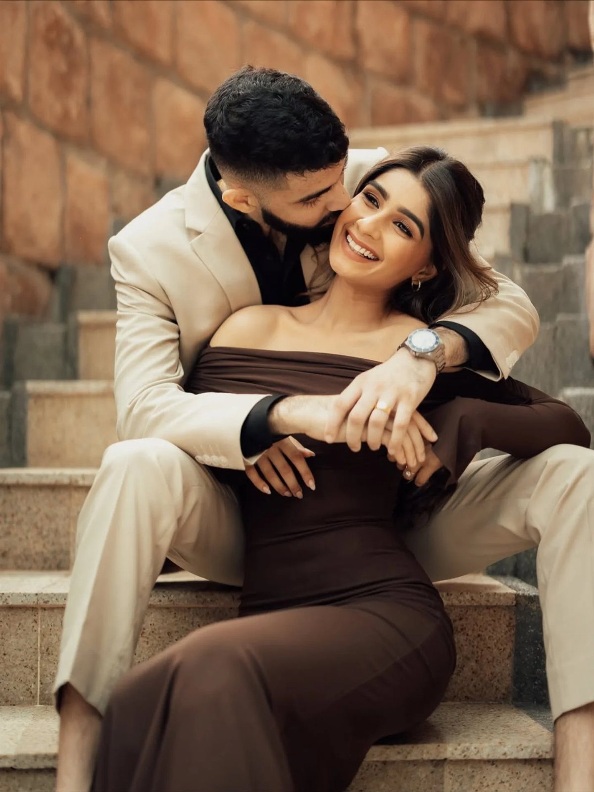 Couple in coordinating beige and brown outfits posing on stone steps.