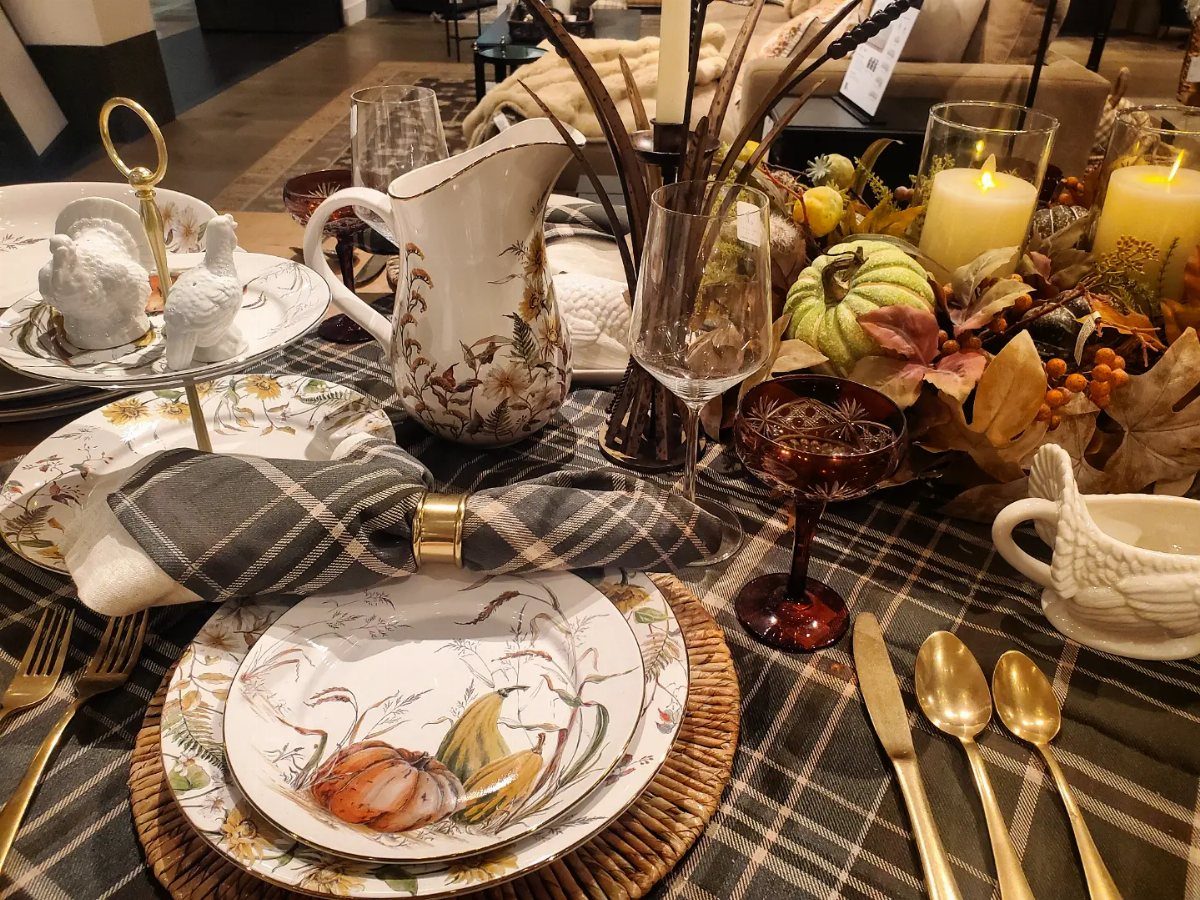 Autumn table setting with pumpkin plates, gold cutlery, and amber glassware on plaid.