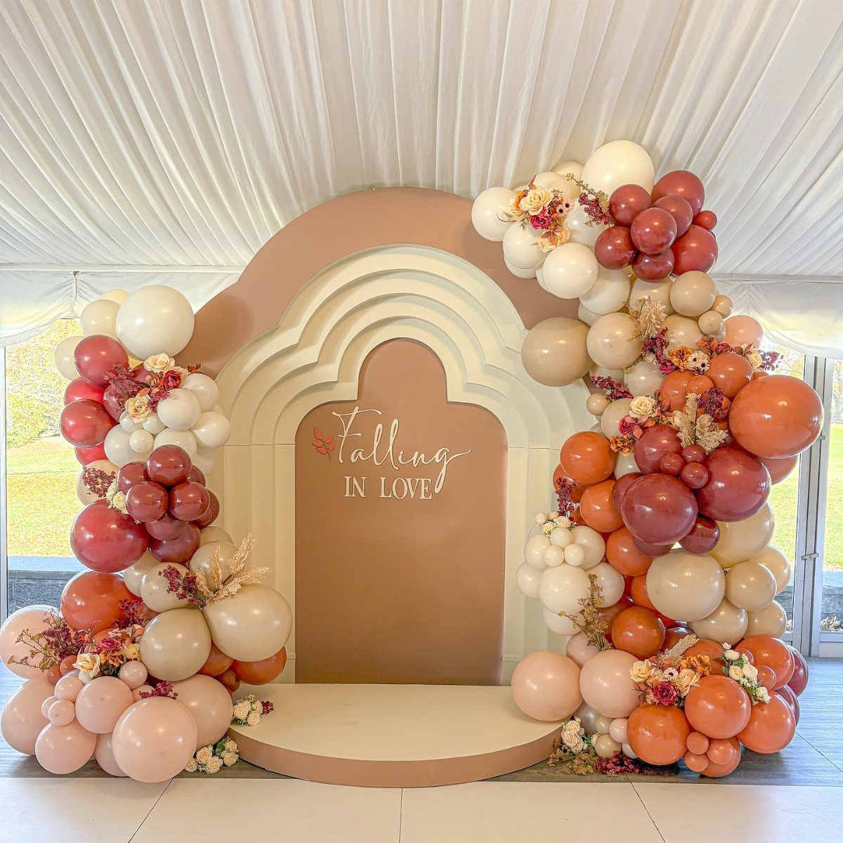 Terracotta arched backdrop with balloon garlands and Falling In Love text for event.