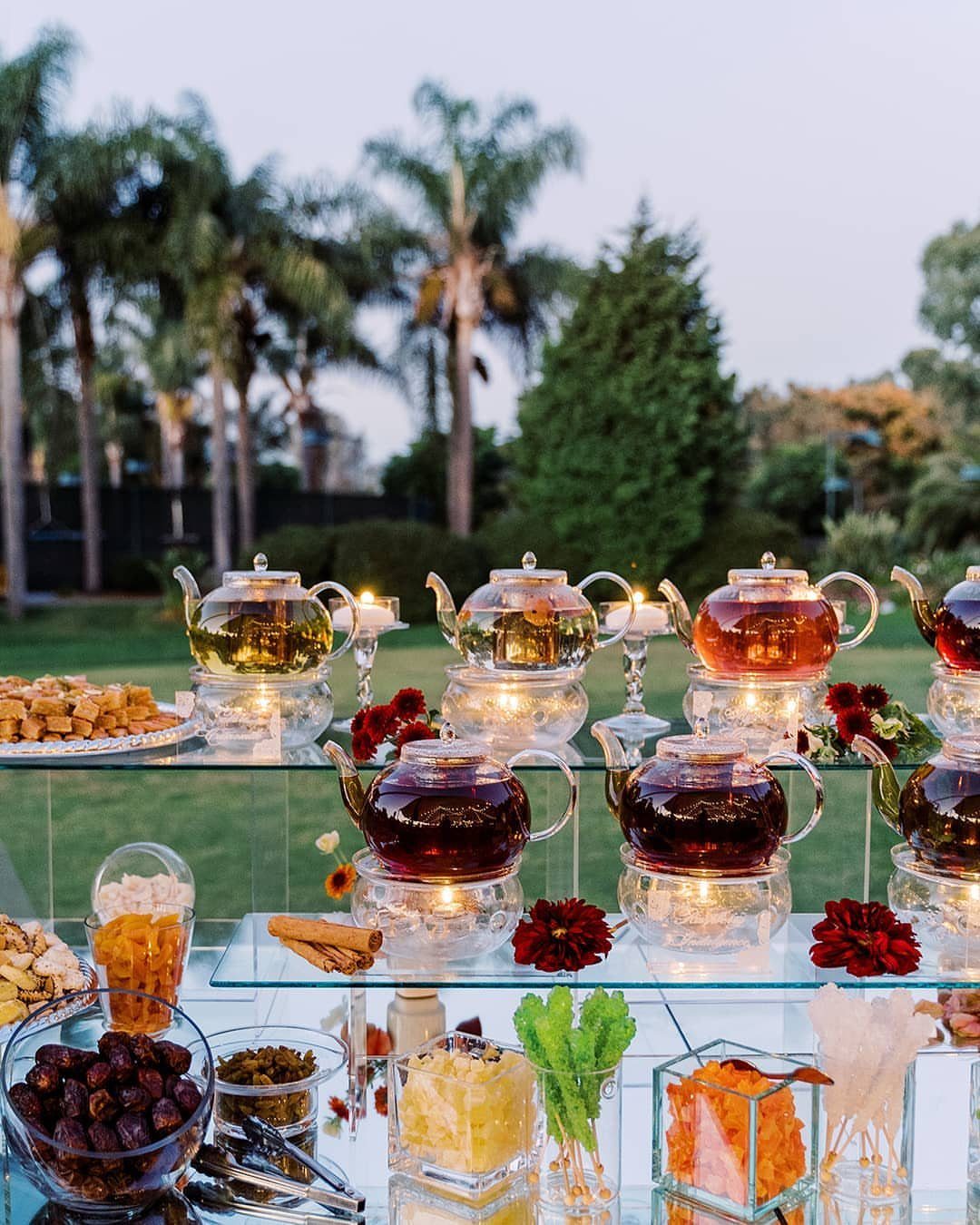 Glass teapots with tea and bowls of dried fruits on outdoor glass shelves.