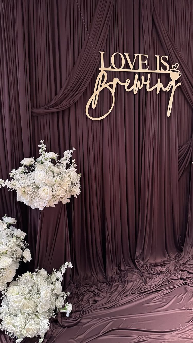 Gold Love is Brewing sign against burgundy draped fabric with white floral arrangements.