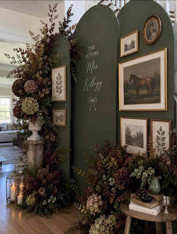 Dark green arched backdrop with autumn flowers, gold framed art, and bridal text.