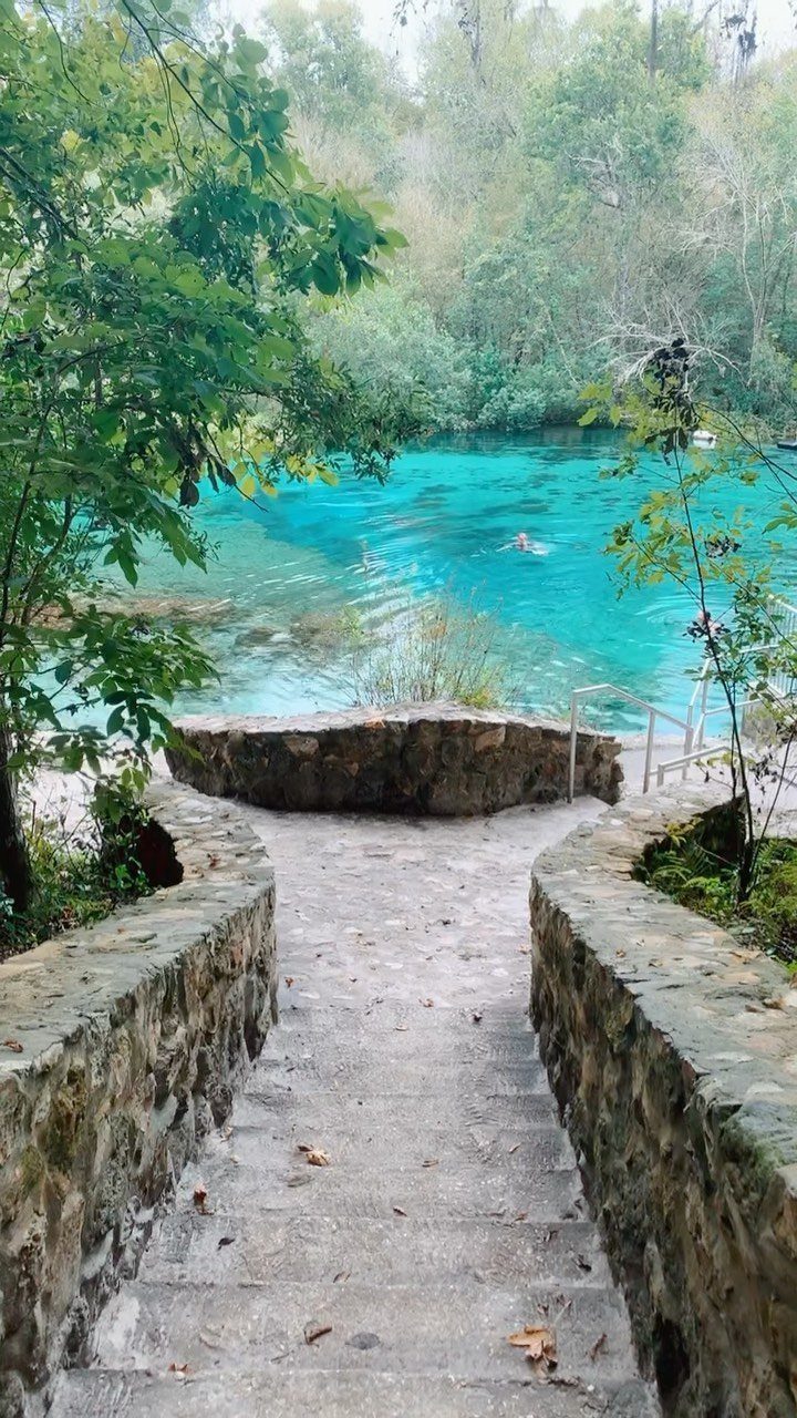 Stone stairs leading down to a vibrant turquoise blue spring surrounded by greenery.