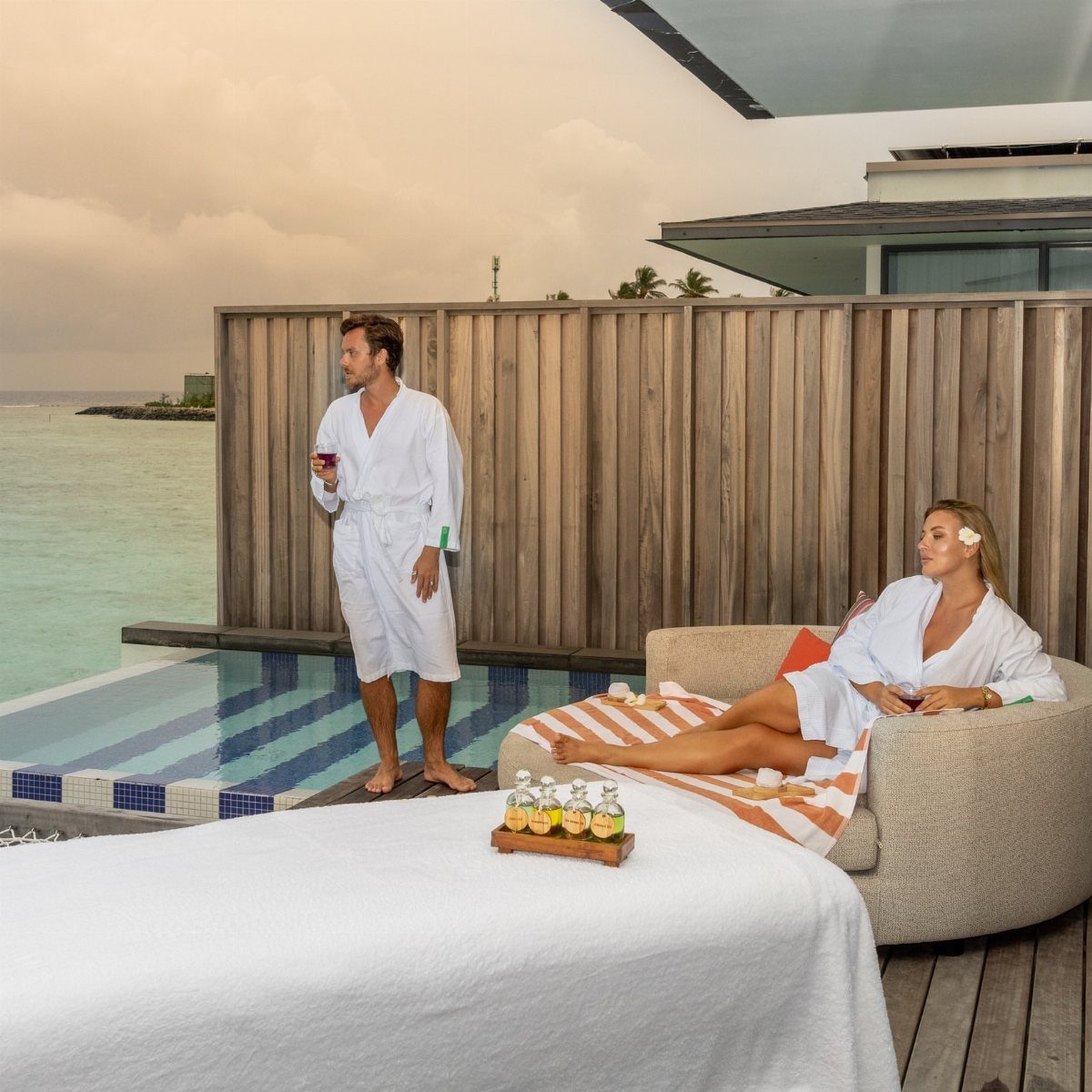 Couple in white robes relaxing on a luxury poolside deck with massage setup.