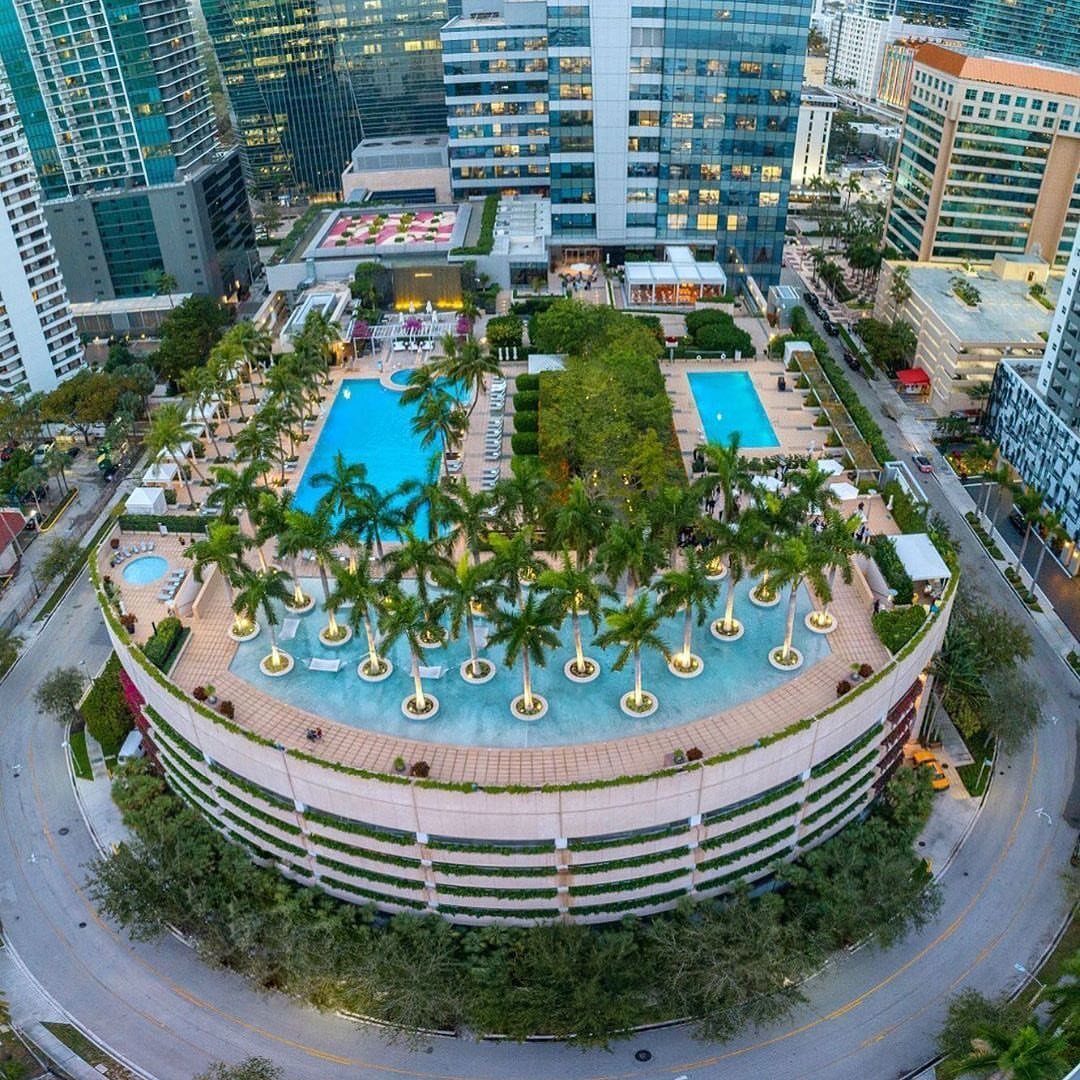 Luxury hotel rooftop with turquoise swimming pools and palm trees amidst city skyscrapers.