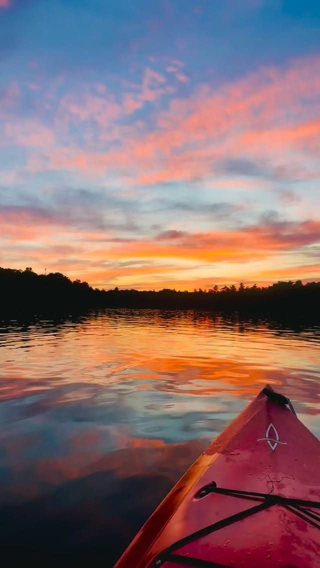 Red kayak bow on calm water reflecting a colorful orange and pink sunset sky.