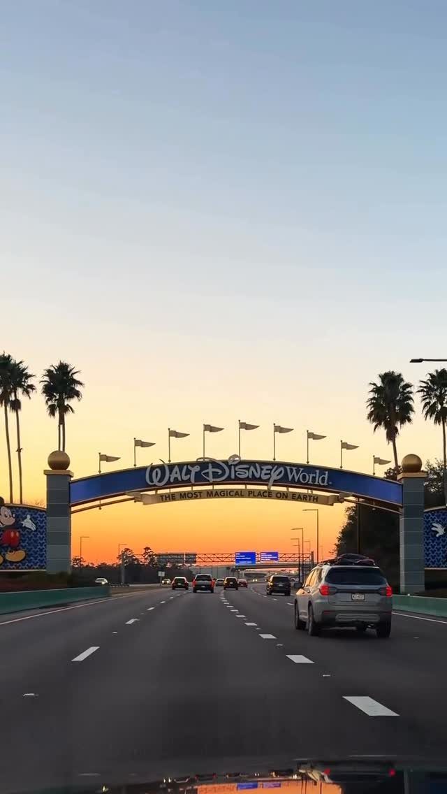 Walt Disney World entrance archway over a highway during a colorful sunset.