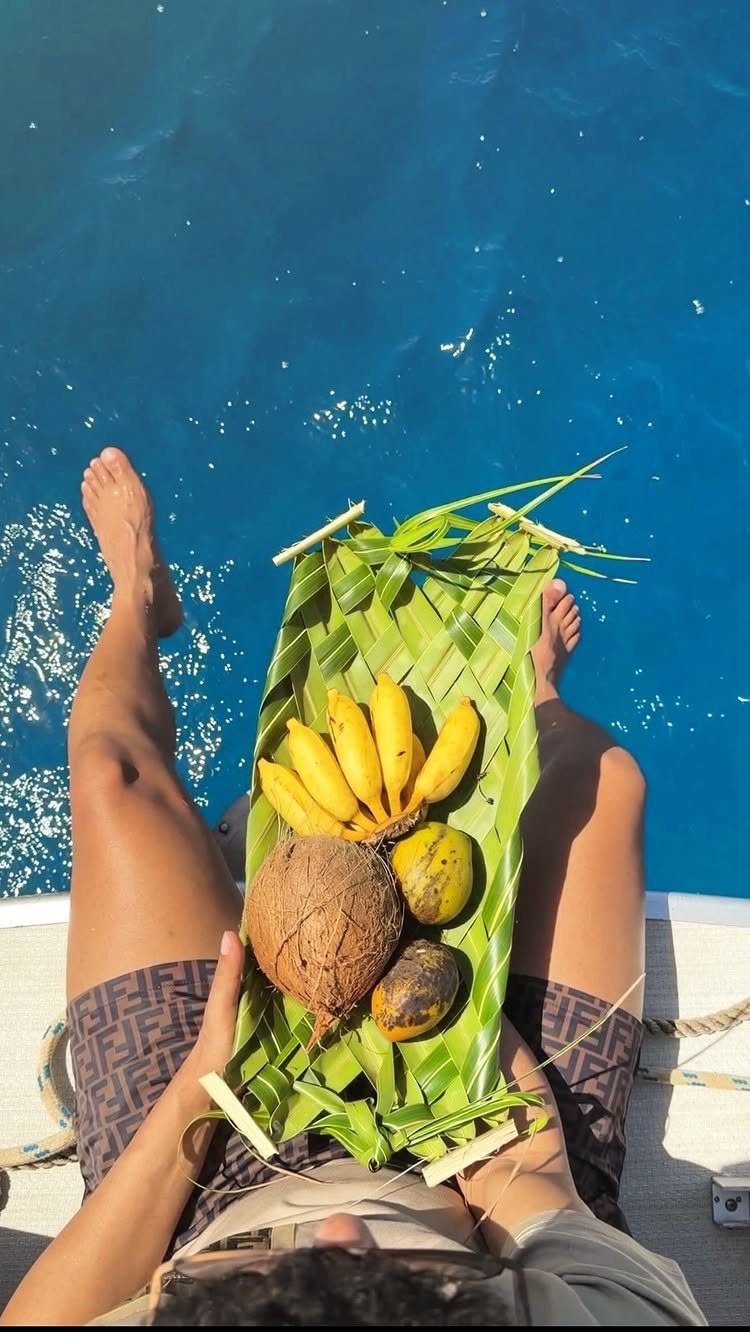 Person on a boat holding a tropical fruit platter over blue ocean water
