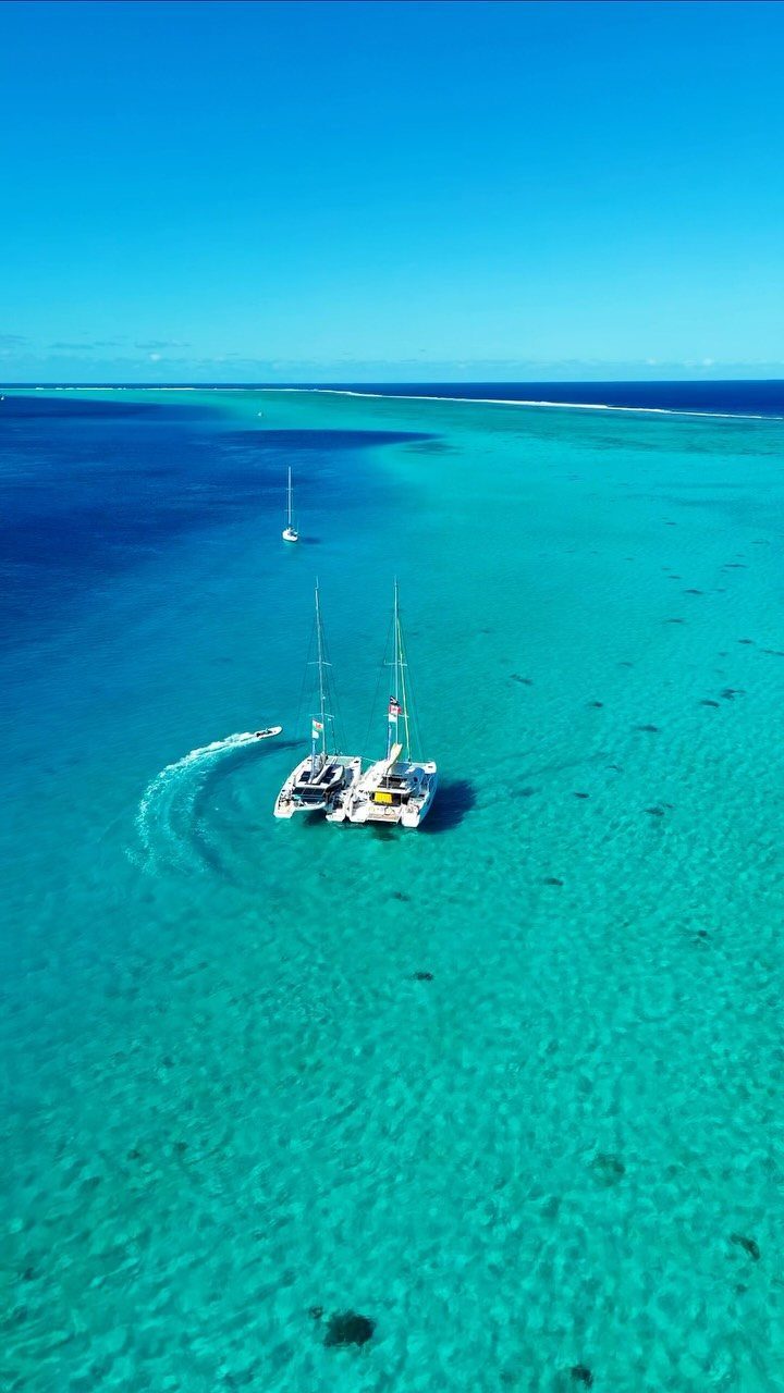 Two white catamarans anchored in a clear turquoise lagoon under a blue sky.