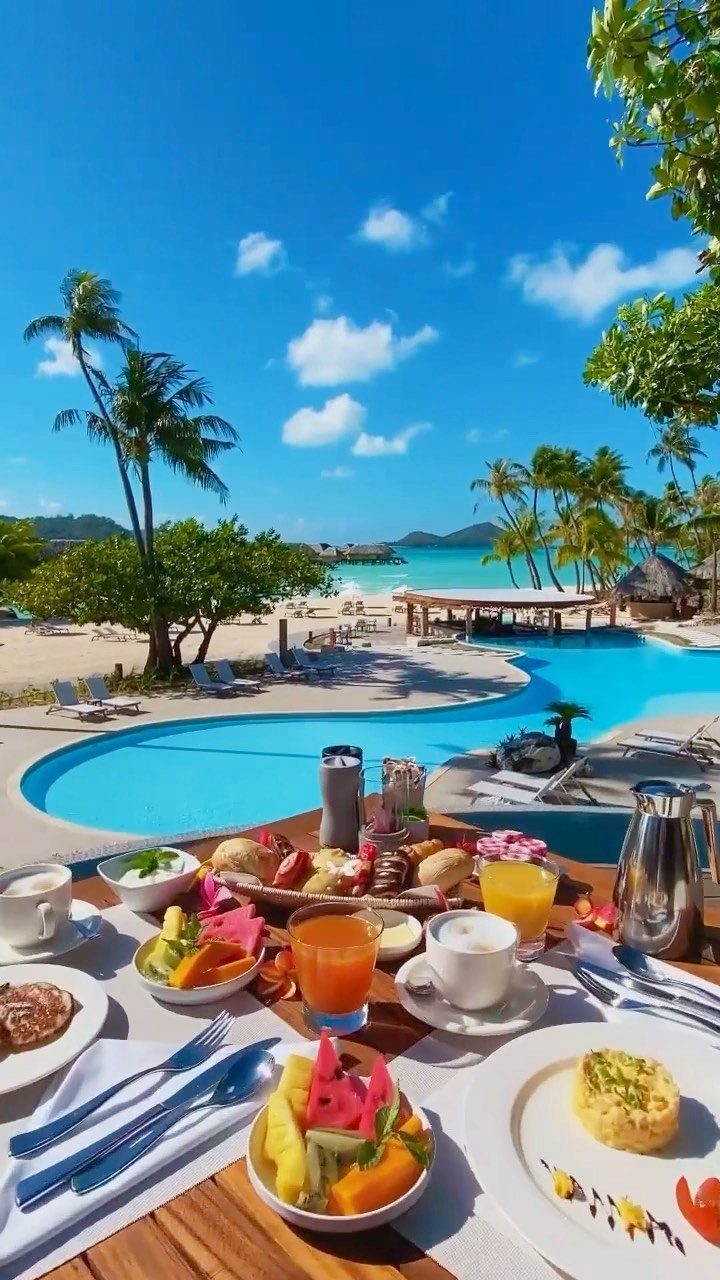 Tropical breakfast spread overlooking a luxury resort pool and white sand beach.