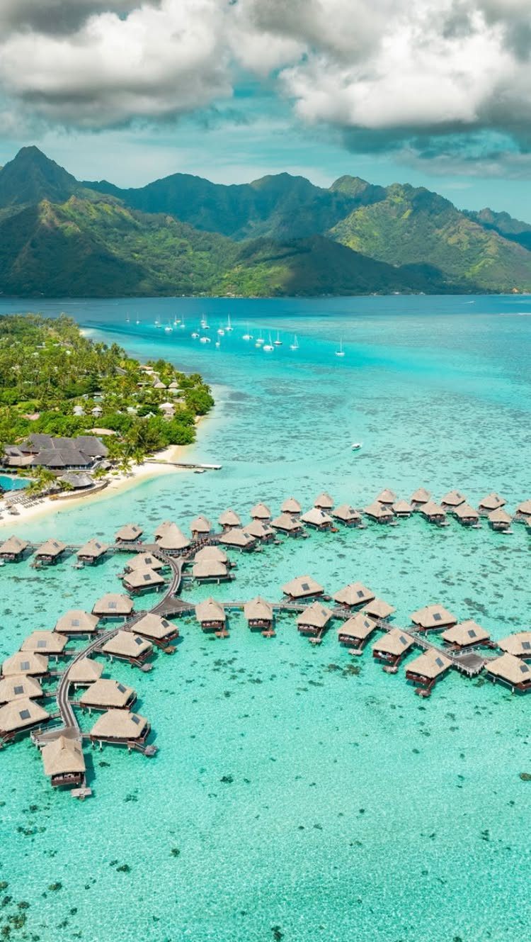 Overwater bungalows with thatched roofs extending into a clear turquoise tropical lagoon.