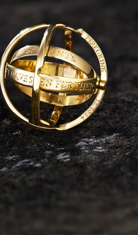 Gold spherical armillary ring with engraved text on a dark stone background