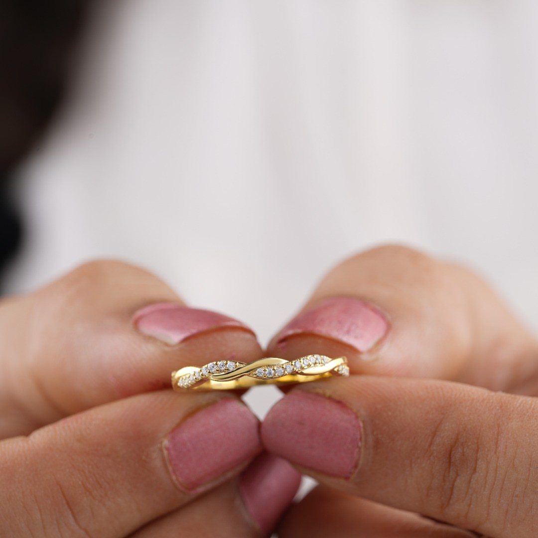 Gold braided wedding ring with small diamonds held by hands with pink nails.