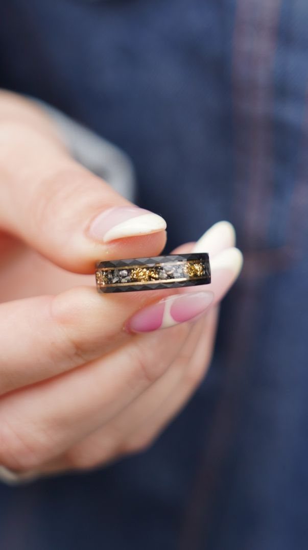 Dark grey wedding band with gold flecks held between two fingers