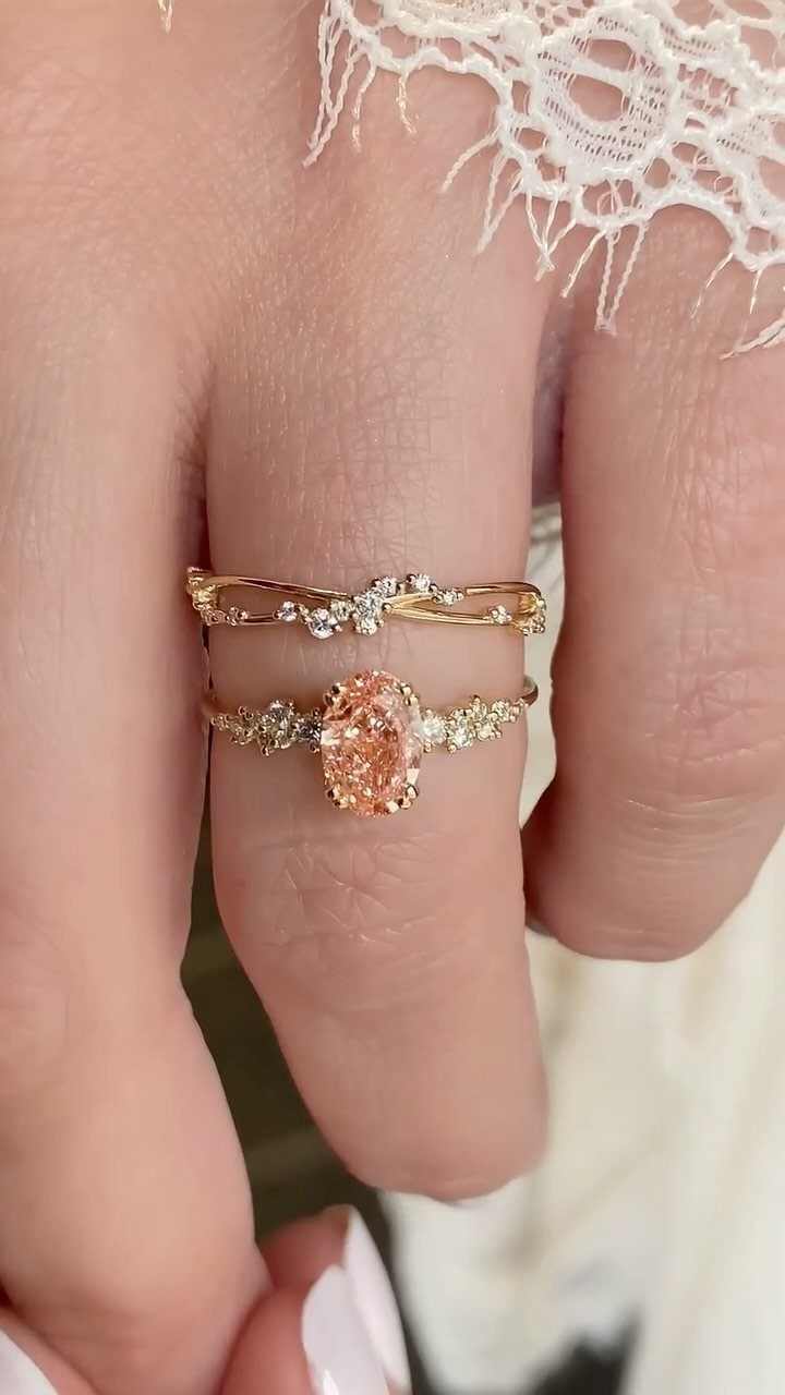 Two gold rings with a peach gemstone and diamonds on a finger