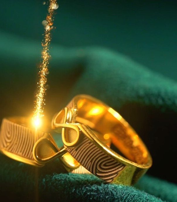Gold wedding bands with fingerprint engravings on green velvet with sparkling gold dust.