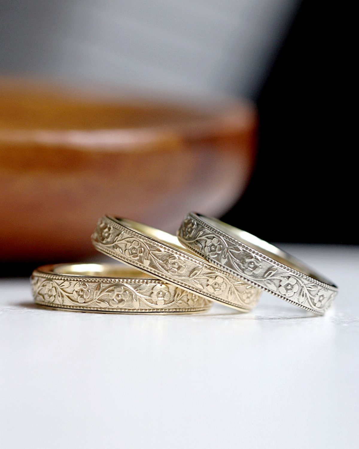 Three gold wedding bands with detailed floral and vine engravings on white surface