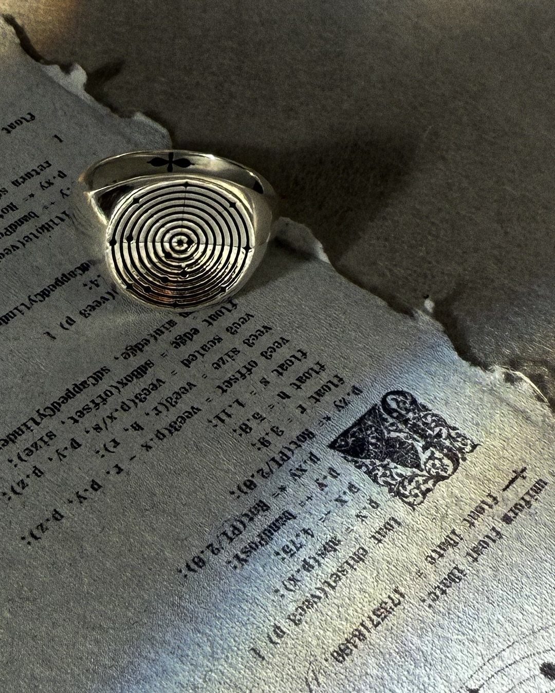 Silver ring with concentric spiral design resting on torn paper with printed code.