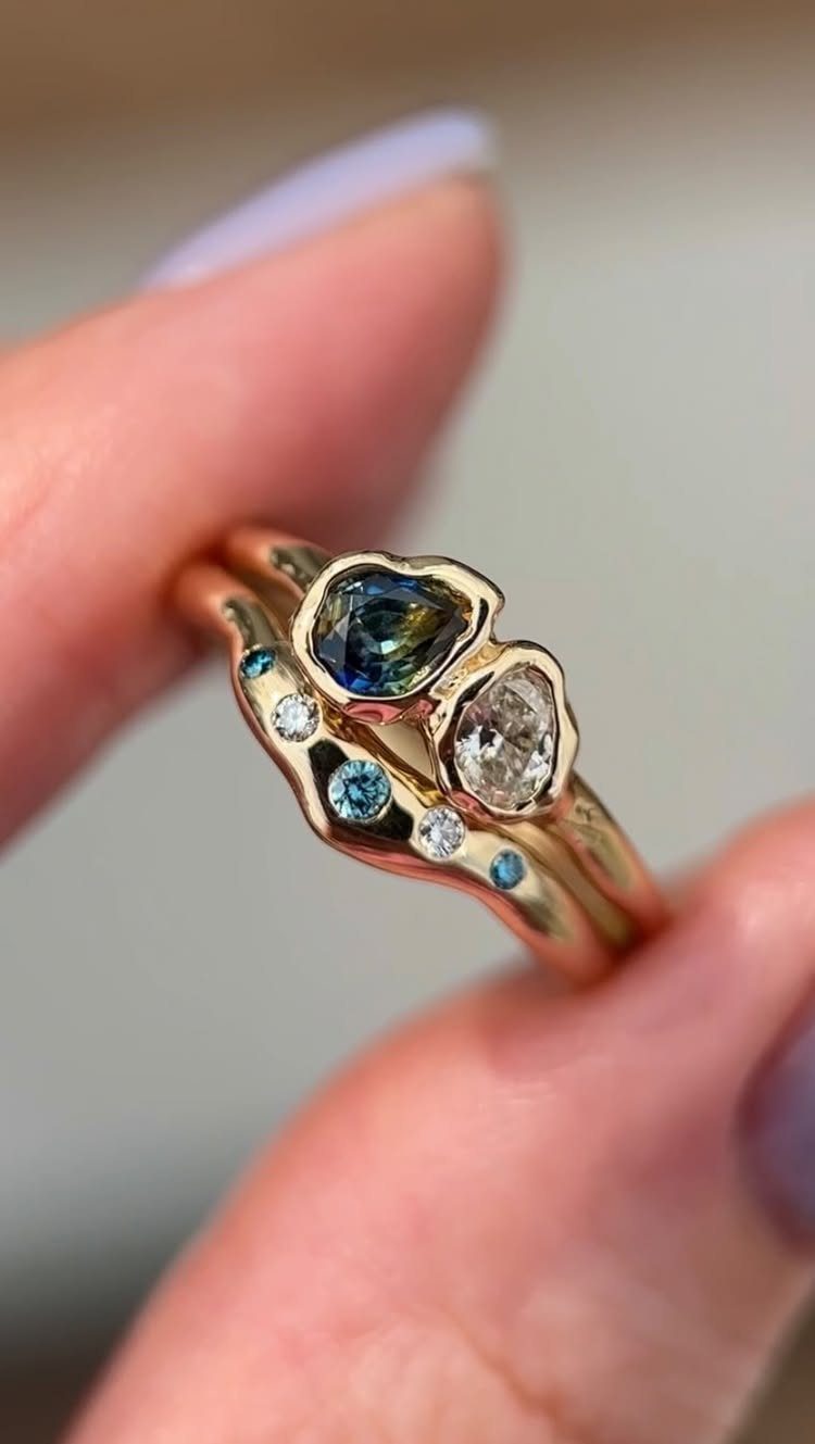 Wavy gold wedding rings with a blue gemstone and clear diamond held by fingers
