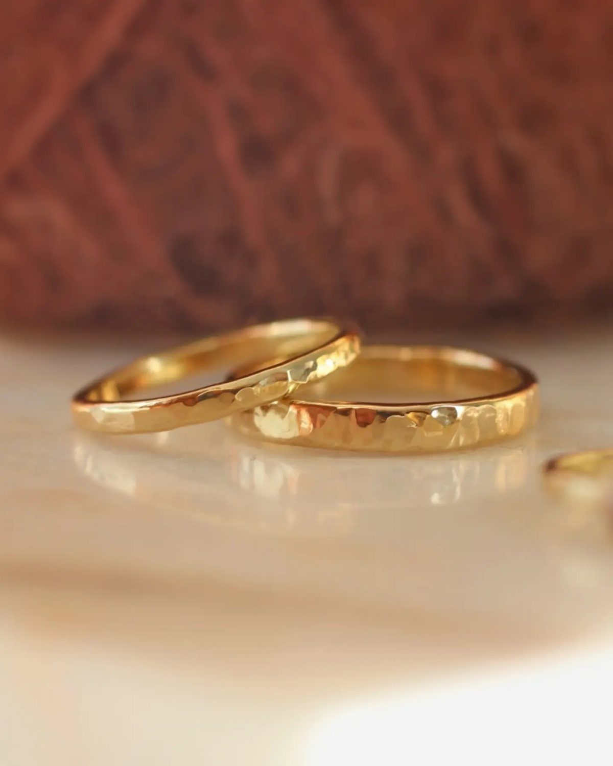 Two hammered gold wedding rings resting on a reflective white surface.