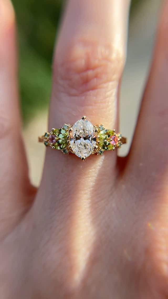 Gold ring with oval diamond and colorful gemstones in a leaf-like design.