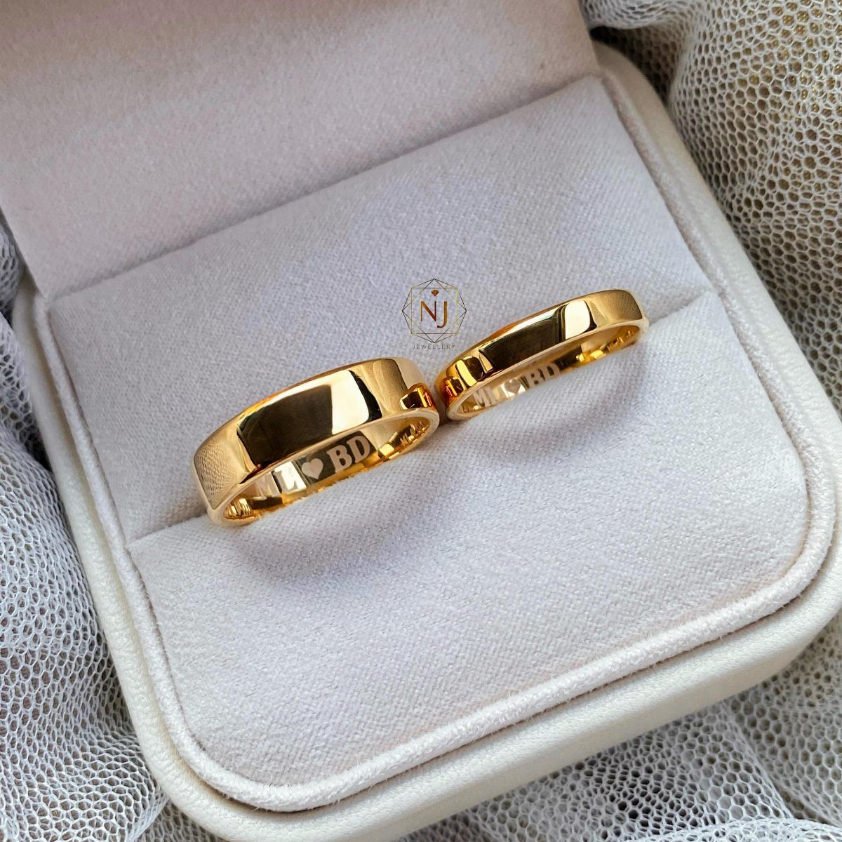 Two gold wedding bands with engravings inside a white velvet jewelry box
