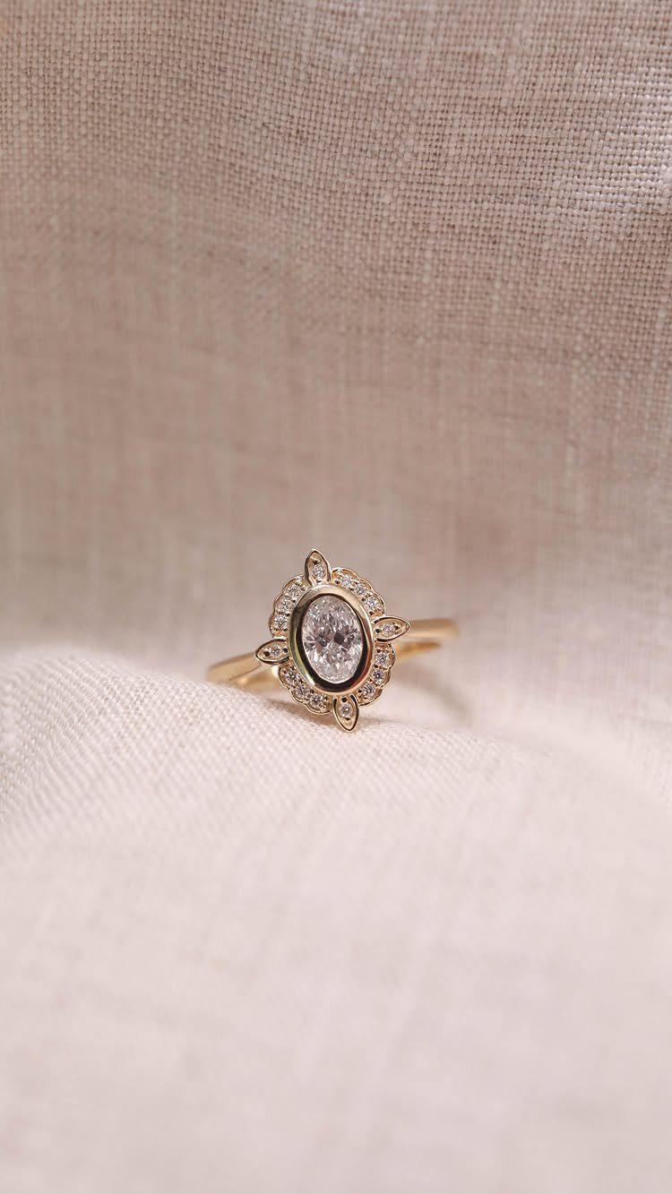 Gold vintage style wedding ring with oval diamond and intricate halo detailing.