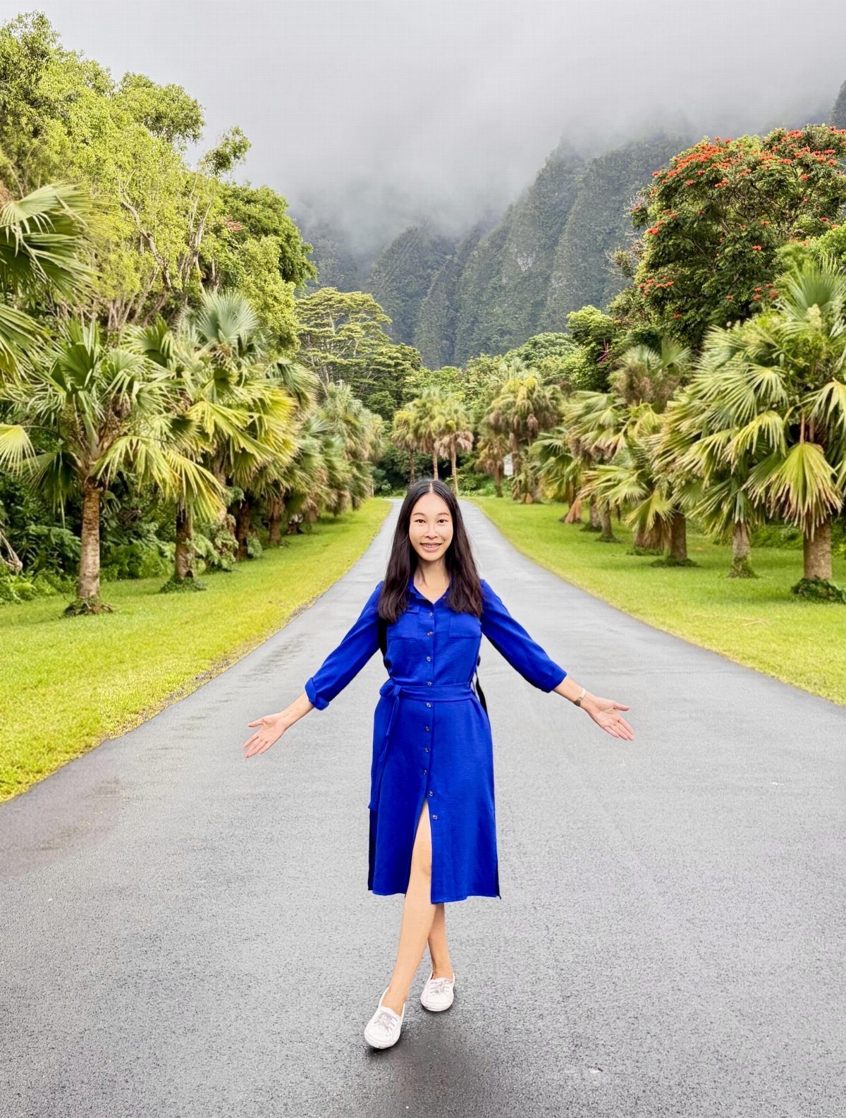 Woman in a royal blue midi dress standing on a tropical road.