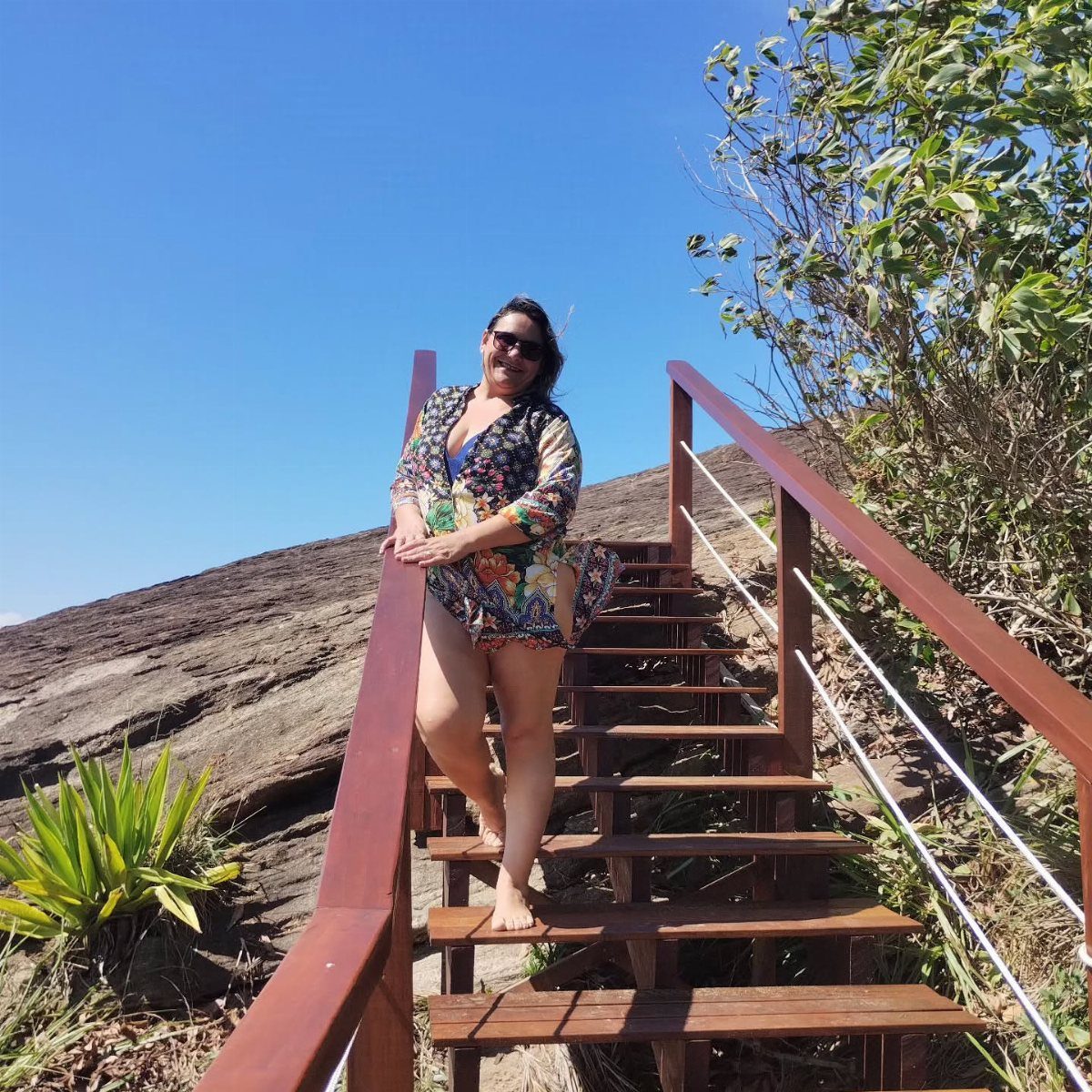 Woman in floral cover-up and sunglasses standing on wooden stairs on a hillside