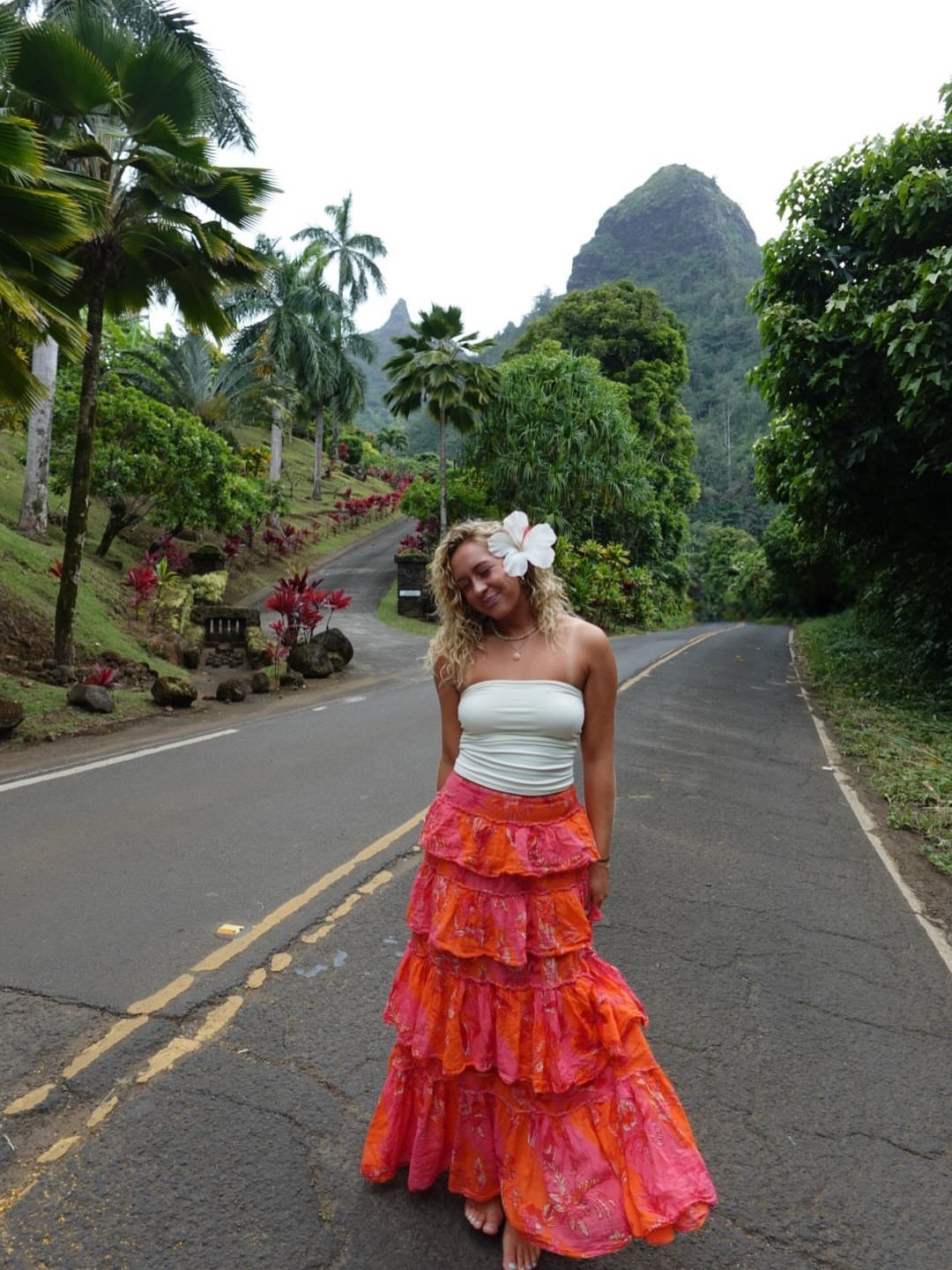 Woman wearing a tiered orange flowy skirt and white top on a tropical road