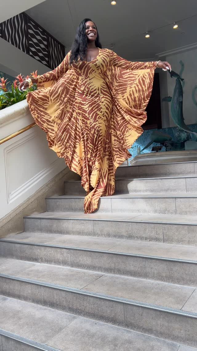 Woman wearing a flowy brown and gold patterned maxi dress on stone stairs