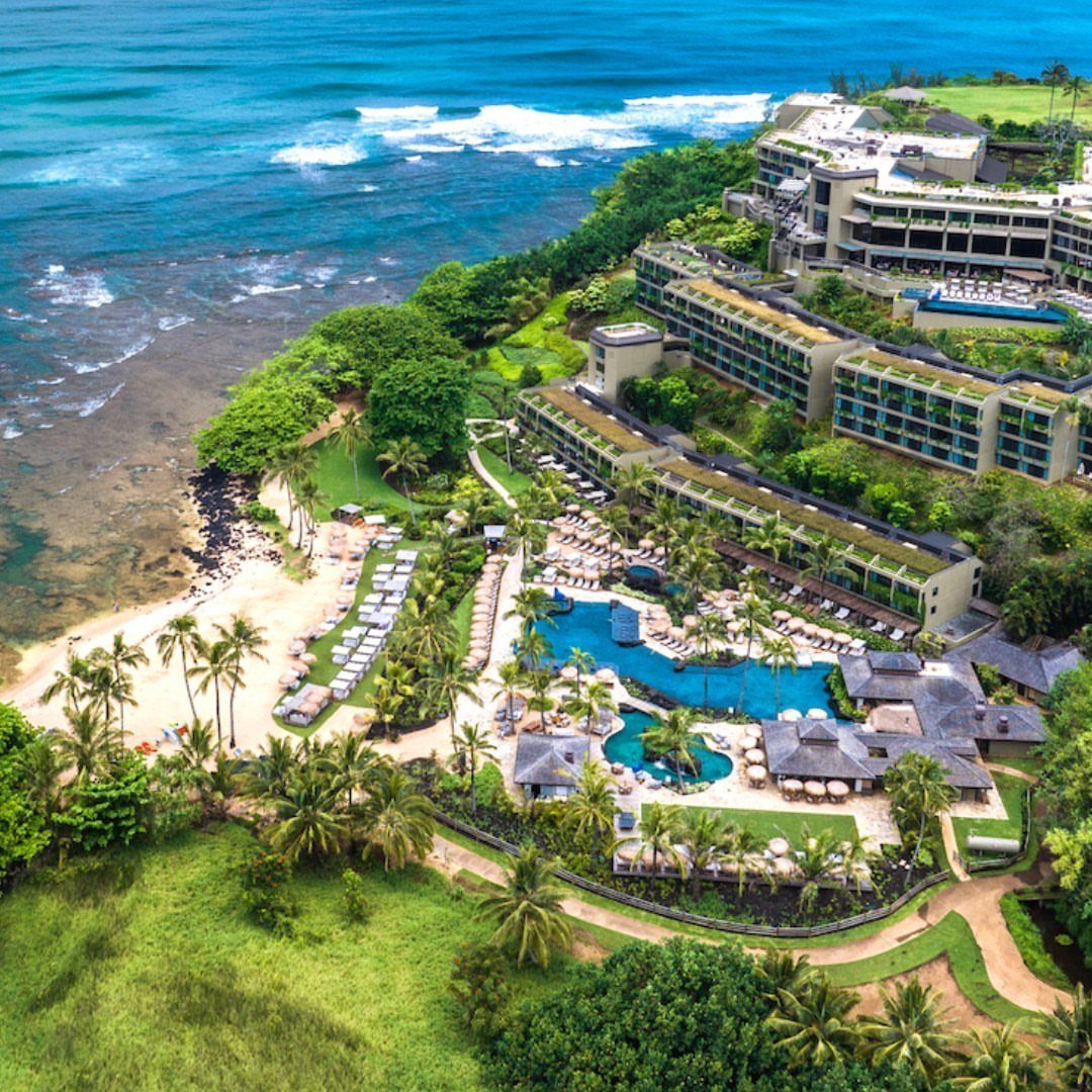 Luxury beachfront resort with green roofs and blue pools overlooking the turquoise ocean.