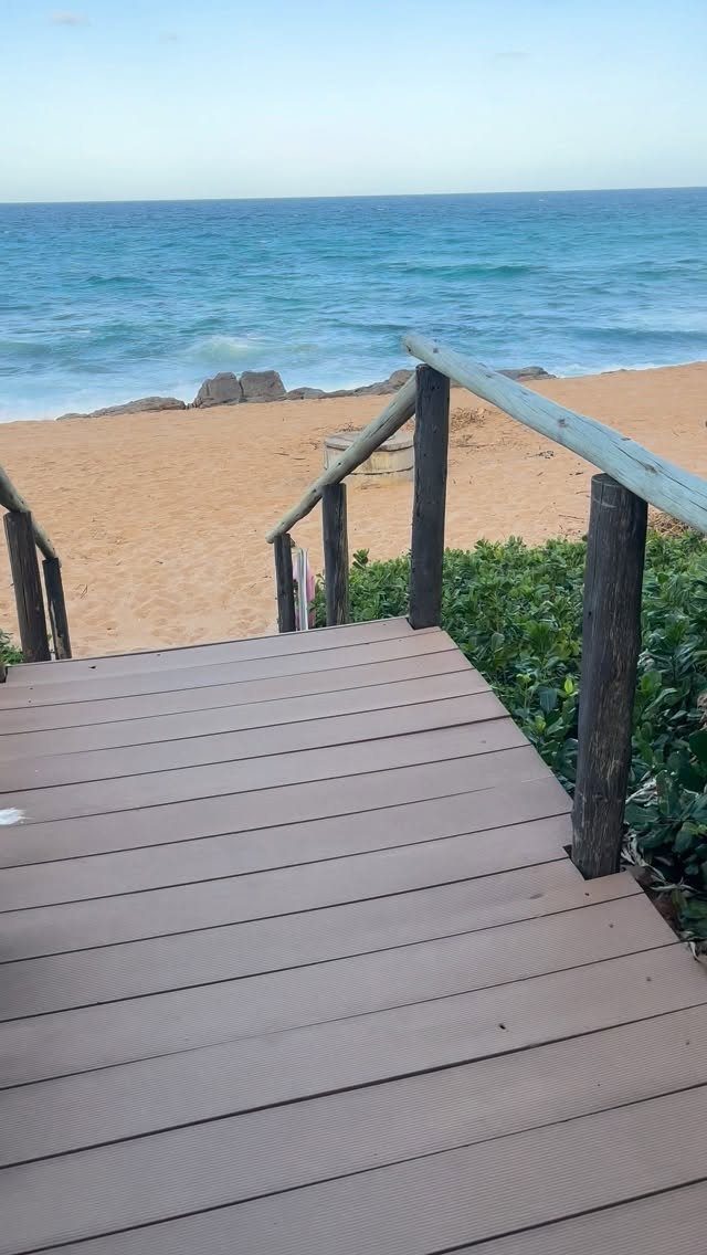 Wooden boardwalk leading directly from a resort area down to a sandy beach.