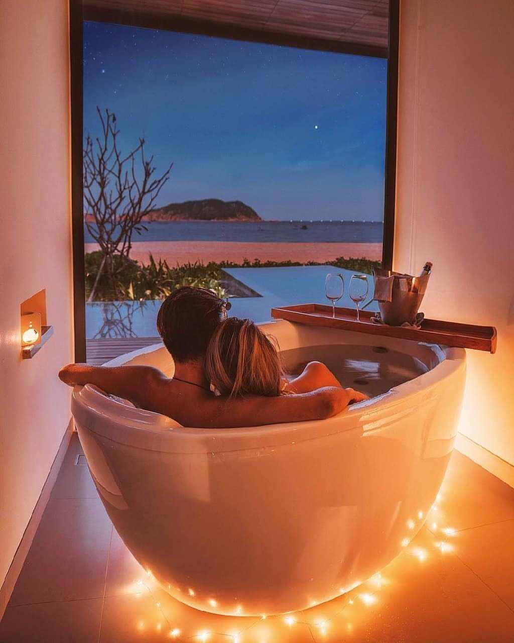 Couple in a bathtub overlooking a private infinity pool and beach at twilight.
