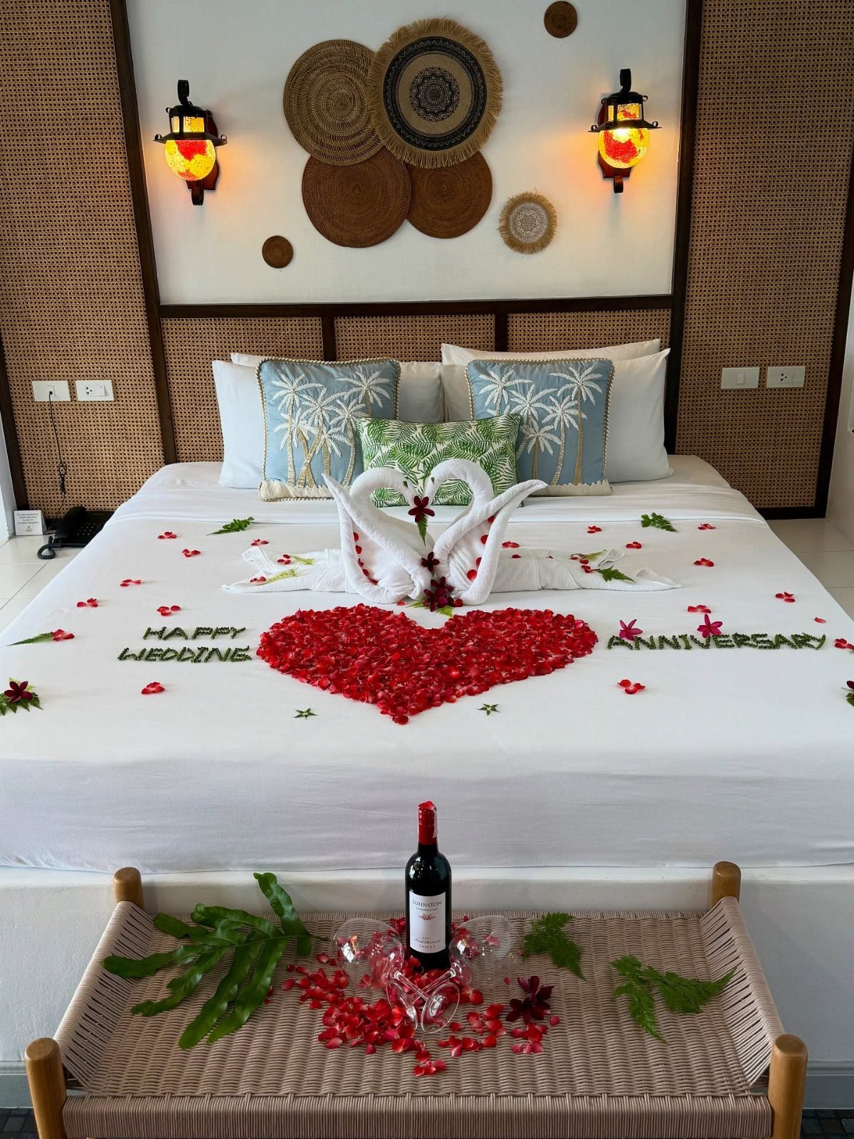 Bed decorated with towel swans and rose petals for a wedding anniversary celebration.