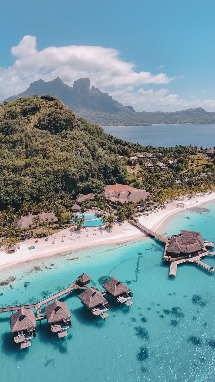 Luxury resort with overwater bungalows and white sand beach against tropical mountains.