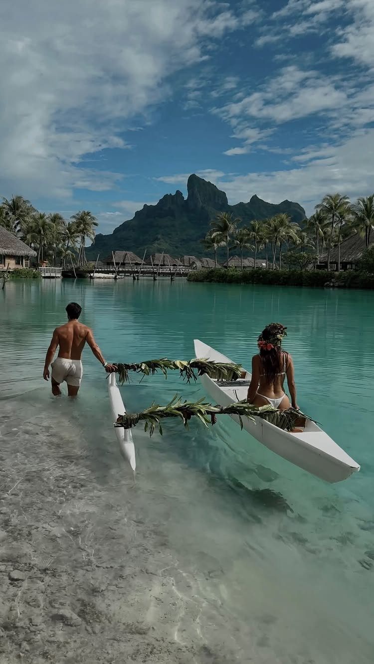 Couple with a white outrigger canoe on a tropical beach with mountain backdrop